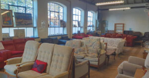 a large collection of chairs and sofas in a room with large windows and a wooden floor